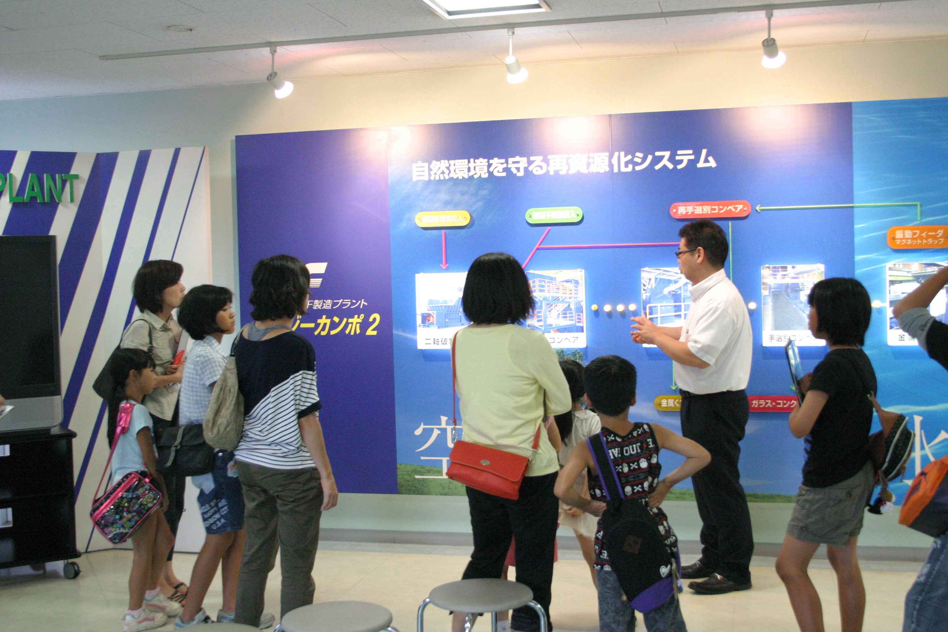 製造ラインの流れの説明を受ける見学者